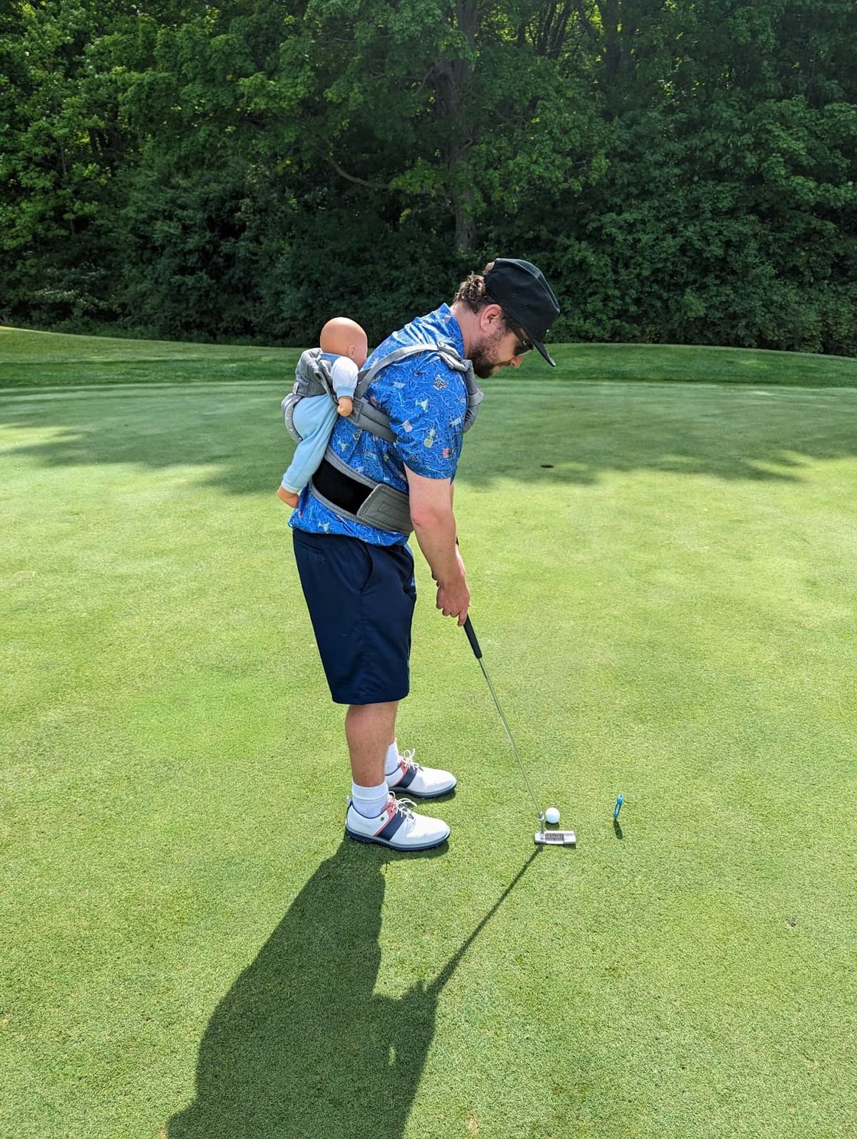 Dad golfing with baby on his back at the annual It's Fore the Kids golf outing